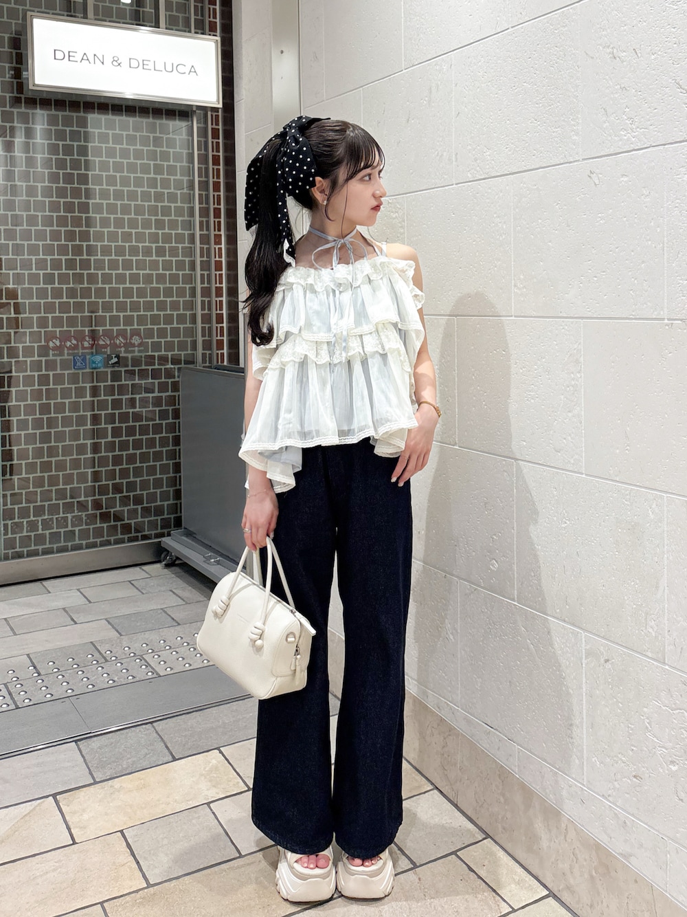 ホワイト系のハンドバッグ、ブルー系のデニムパンツ、ホワイト系のトップスを着用したレディースの夏コーディネートの1枚目の写真