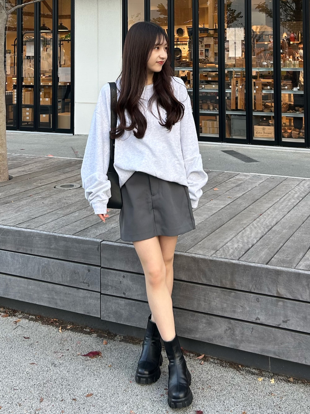 グレー系のスカート、グレー系のスウェット、ブラック系のブーツを着用したレディースの秋コーディネートの1枚目の写真