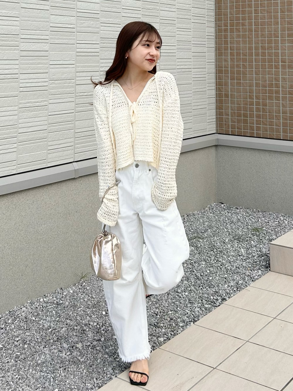 ホワイト系のデニムパンツ、ホワイト系のニット/セーター、ゴールド系のショルダーバッグを着用したレディースの春コーディネートの1枚目の写真