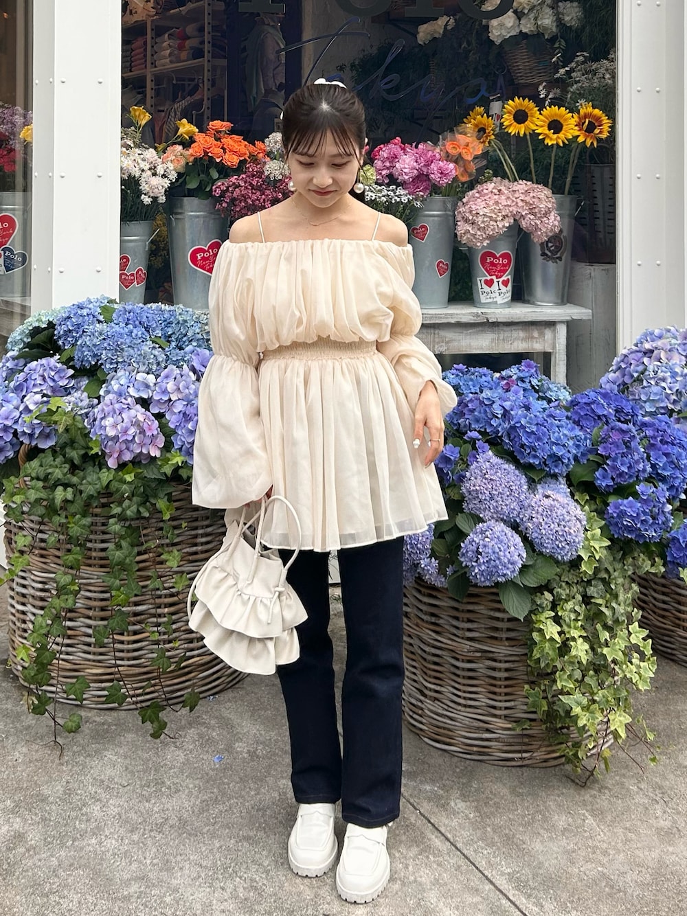 ブルー系のデニムパンツ、ホワイト系のトップス、ホワイト系のショルダーバッグを着用したレディースの春コーディネートの1枚目の写真