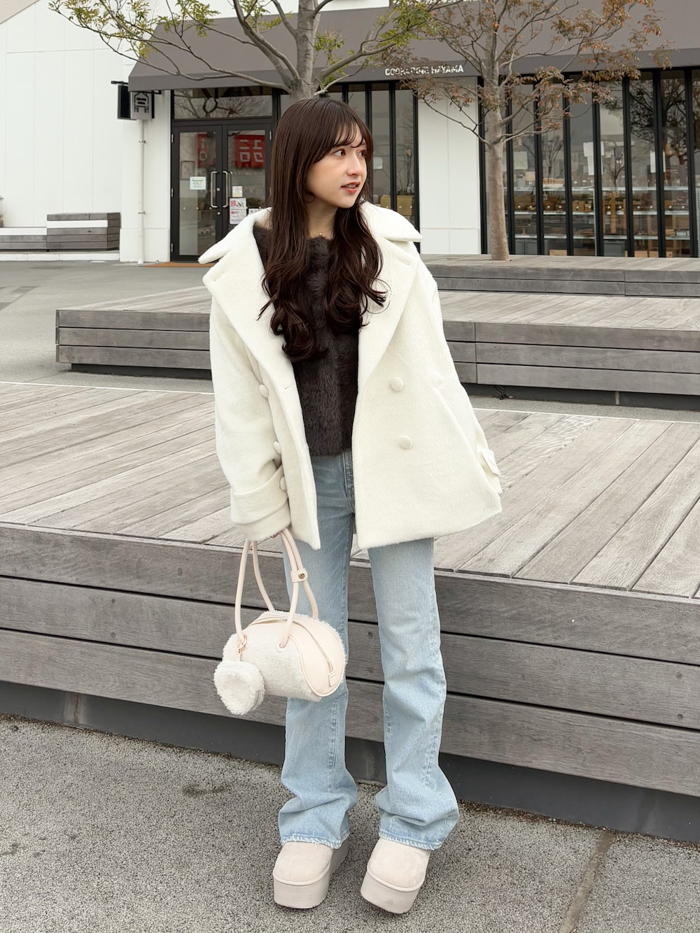 ブラウン系のカーディガン/ボレロ、ブルー系のデニムパンツ、ホワイト系のボストンバッグを着用したレディースの春コーディネートの1枚目の写真