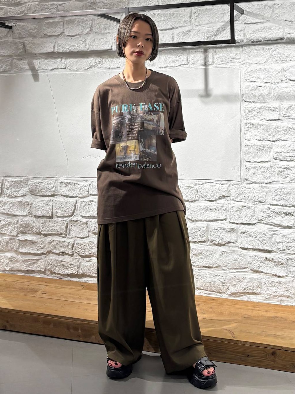 グリーン系のスラックス、ブラウン系のTシャツ/カットソー、ブラック系のサンダルを着用したレディースの夏コーディネートの1枚目の写真