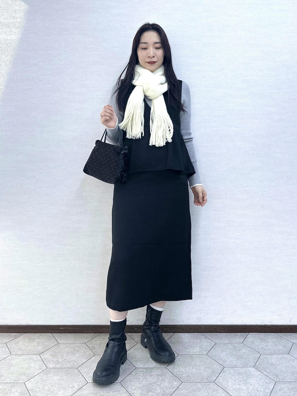 グレー系のニット/セーター、ブラック系のハンドバッグ、ブラック系のジャンパースカートを着用したレディースの冬コーディネートの1枚目の写真