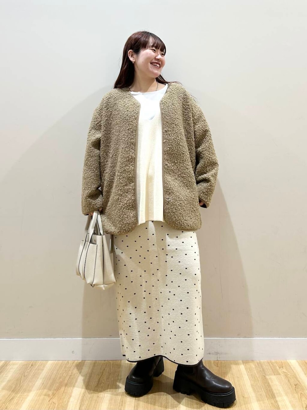 ブラウン系のハンドバッグ、ブラウン系のノーカラーコート、ホワイト系のスカートを着用したレディースの冬コーディネートの1枚目の写真