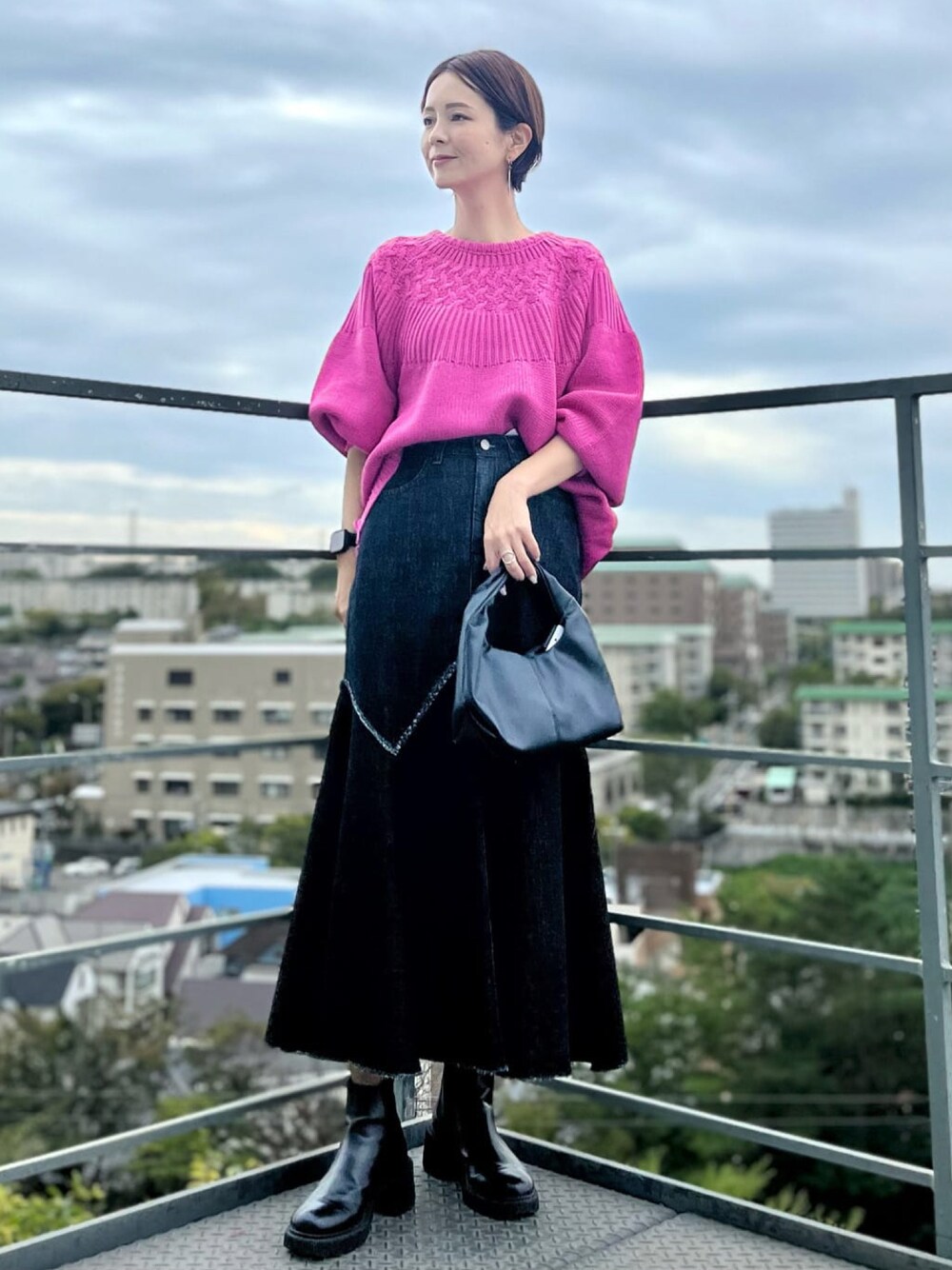 ブラック系のデニムスカート、ブラック系のハンドバッグ、ピンク系のニット/セーターを着用したレディースの秋コーディネートの1枚目の写真