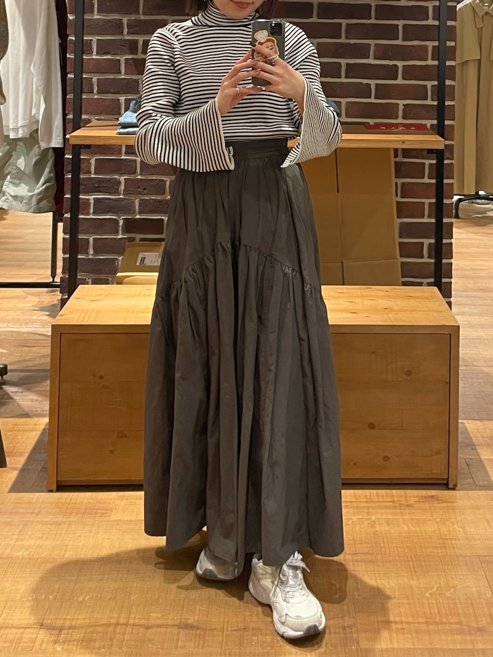 グレー系のスカート、ホワイト系のニット/セーター、シルバー系のショルダーバッグを着用したレディースの冬コーディネートの1枚目の写真