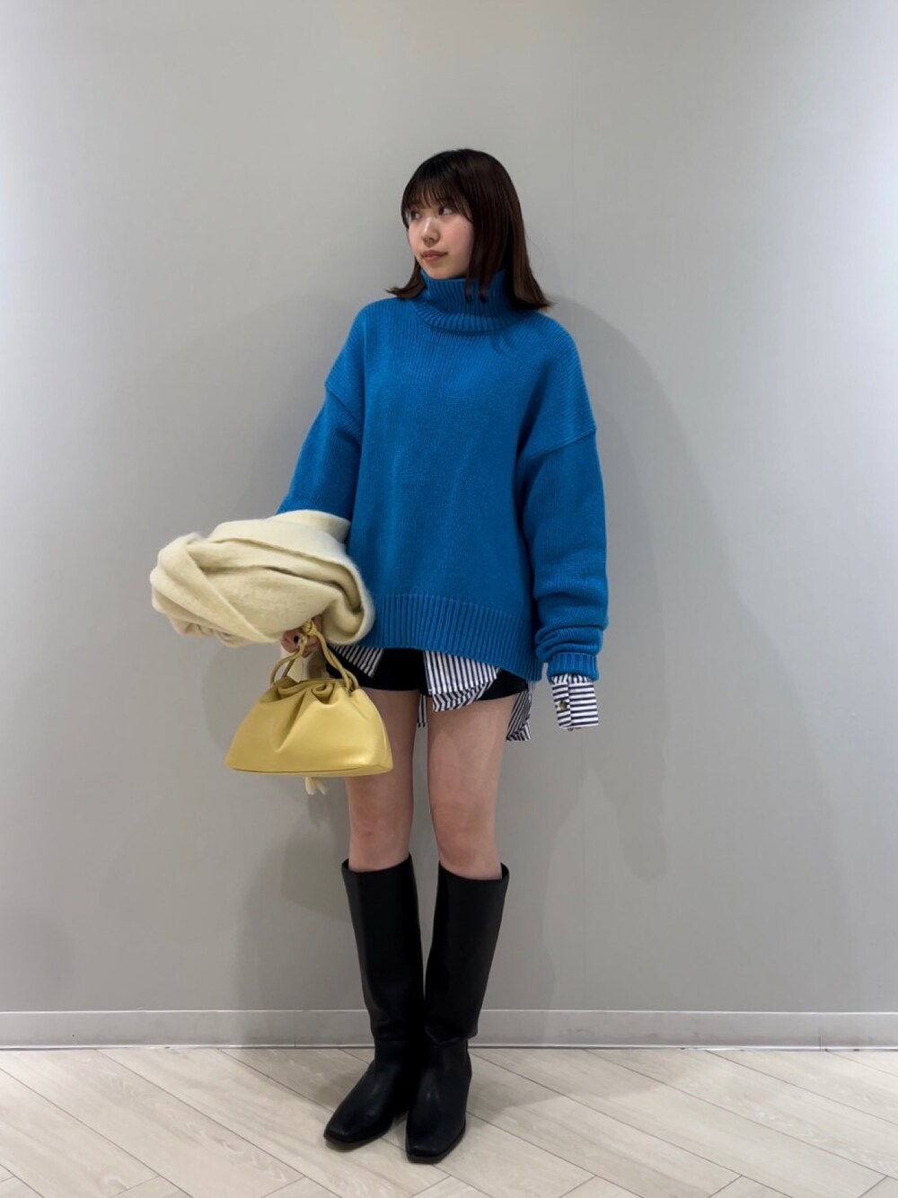ブルー系のニット/セーター、イエロー系のクラッチバッグ、ブラック系のシューズを着用したレディースの冬コーディネートの1枚目の写真