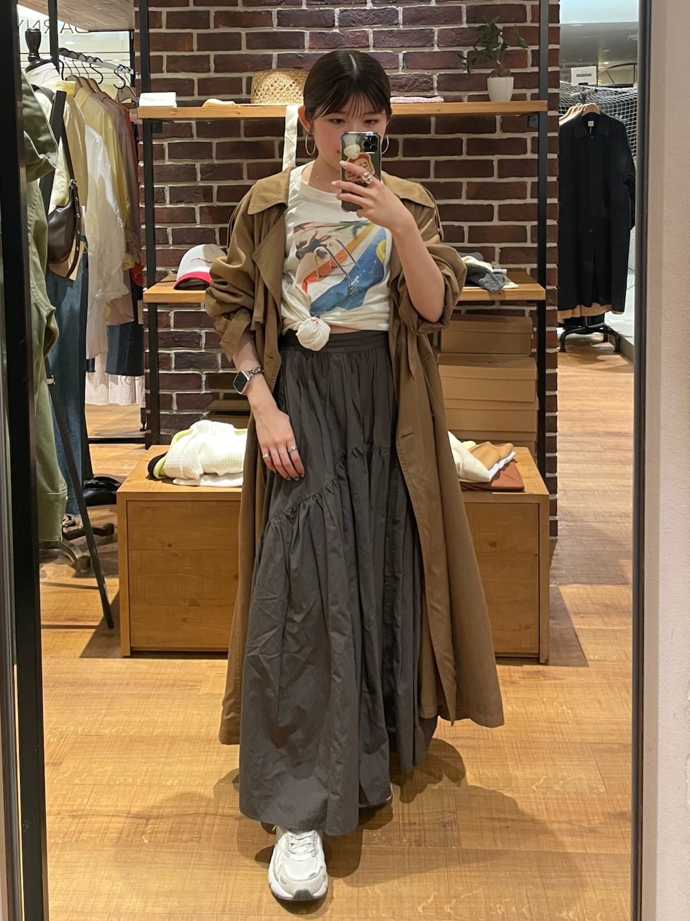 イエロー系のトレンチコート、グレー系のスカート、ホワイト系のTシャツ/カットソーを着用したレディースの春コーディネートの1枚目の写真