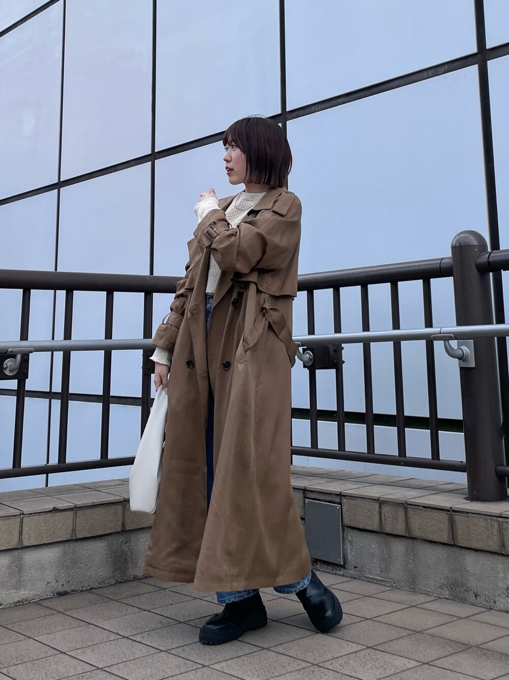 ホワイト系のハンドバッグ、ホワイト系のTシャツ/カットソー、ブルー系のデニムパンツを着用したレディースの冬コーディネートの1枚目の写真