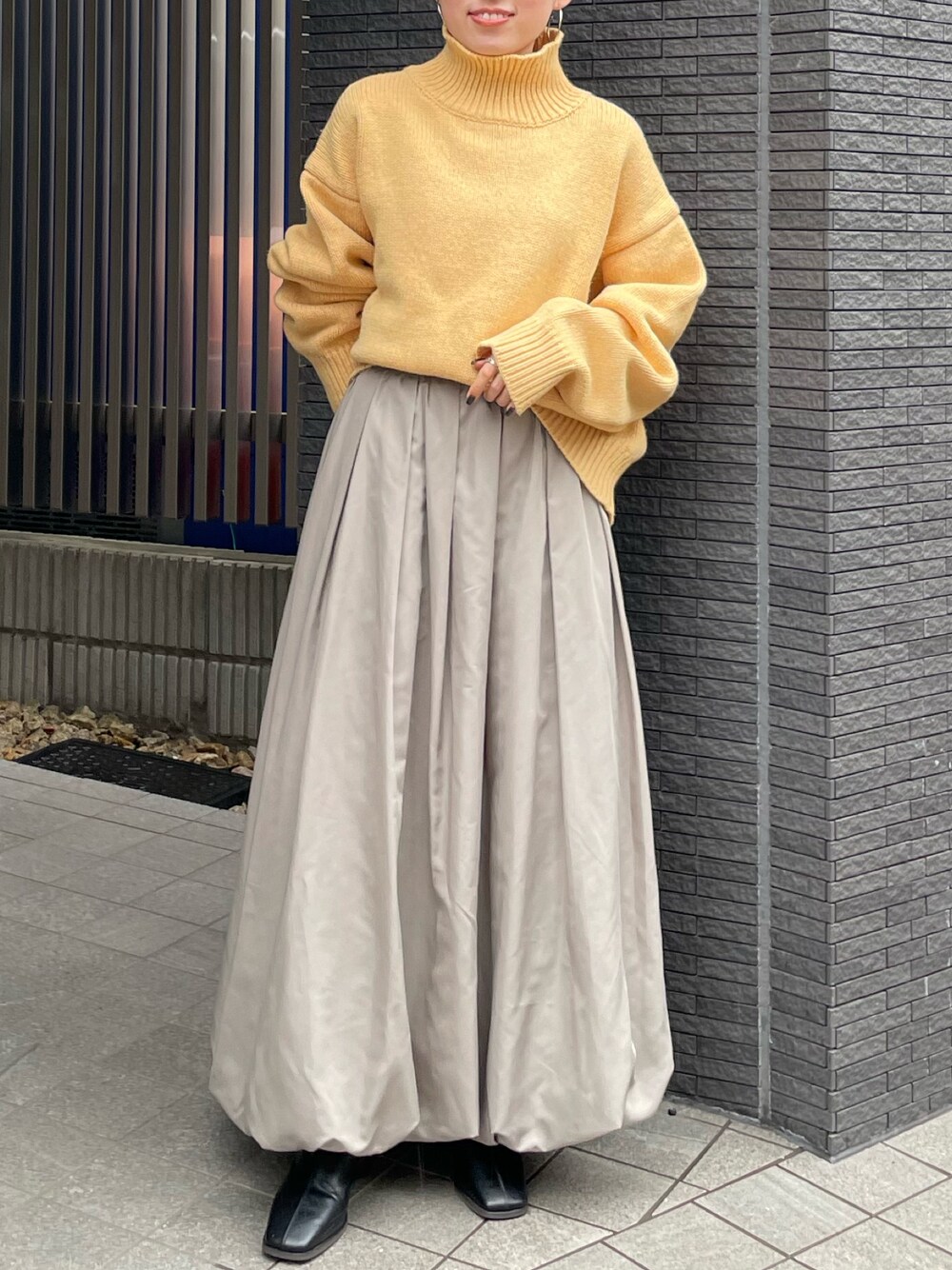 ブラック系のブーツ、イエロー系のニット/セーター、グレー系のスカートを着用したレディースの冬コーディネートの1枚目の写真