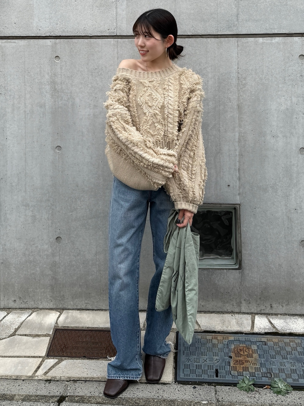 ブルー系のデニムパンツ、グリーン系のトートバッグ、ブラウン系のブーツを着用したレディースの秋コーディネートの1枚目の写真