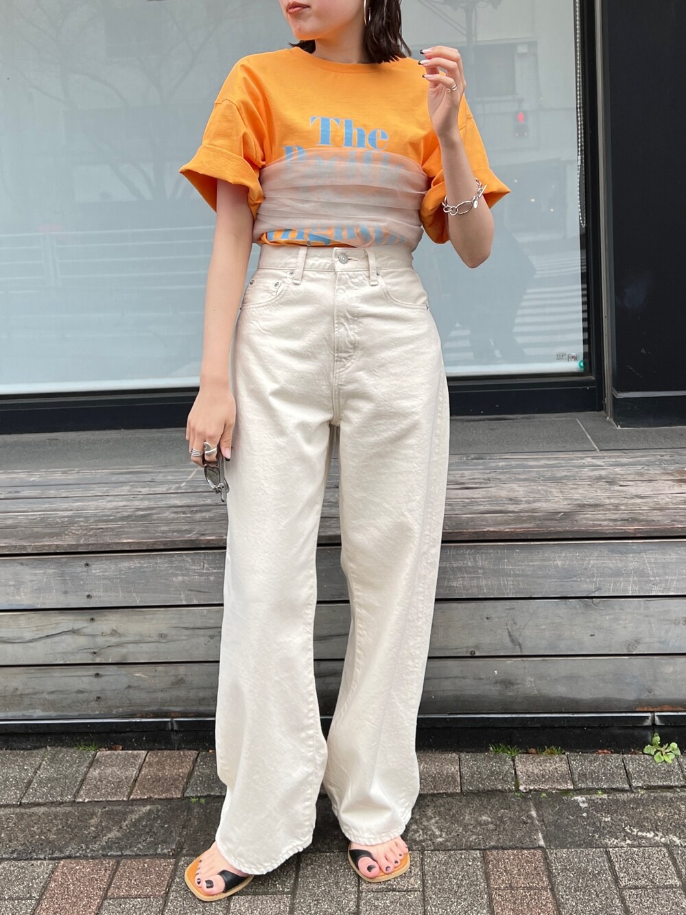 ホワイト系のデニムパンツ、ブラック系のサンダル、オレンジ系のTシャツ/カットソーを着用したレディースの春コーディネートの1枚目の写真