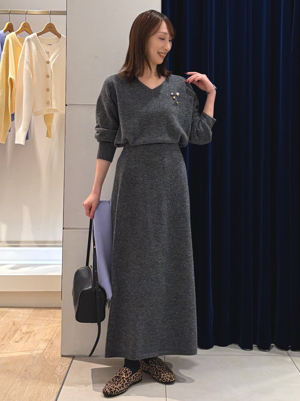 グレー系のニット/セーター、グレー系のスカート、ブラック系のショルダーバッグを着用したレディースの冬コーディネートの1枚目の写真