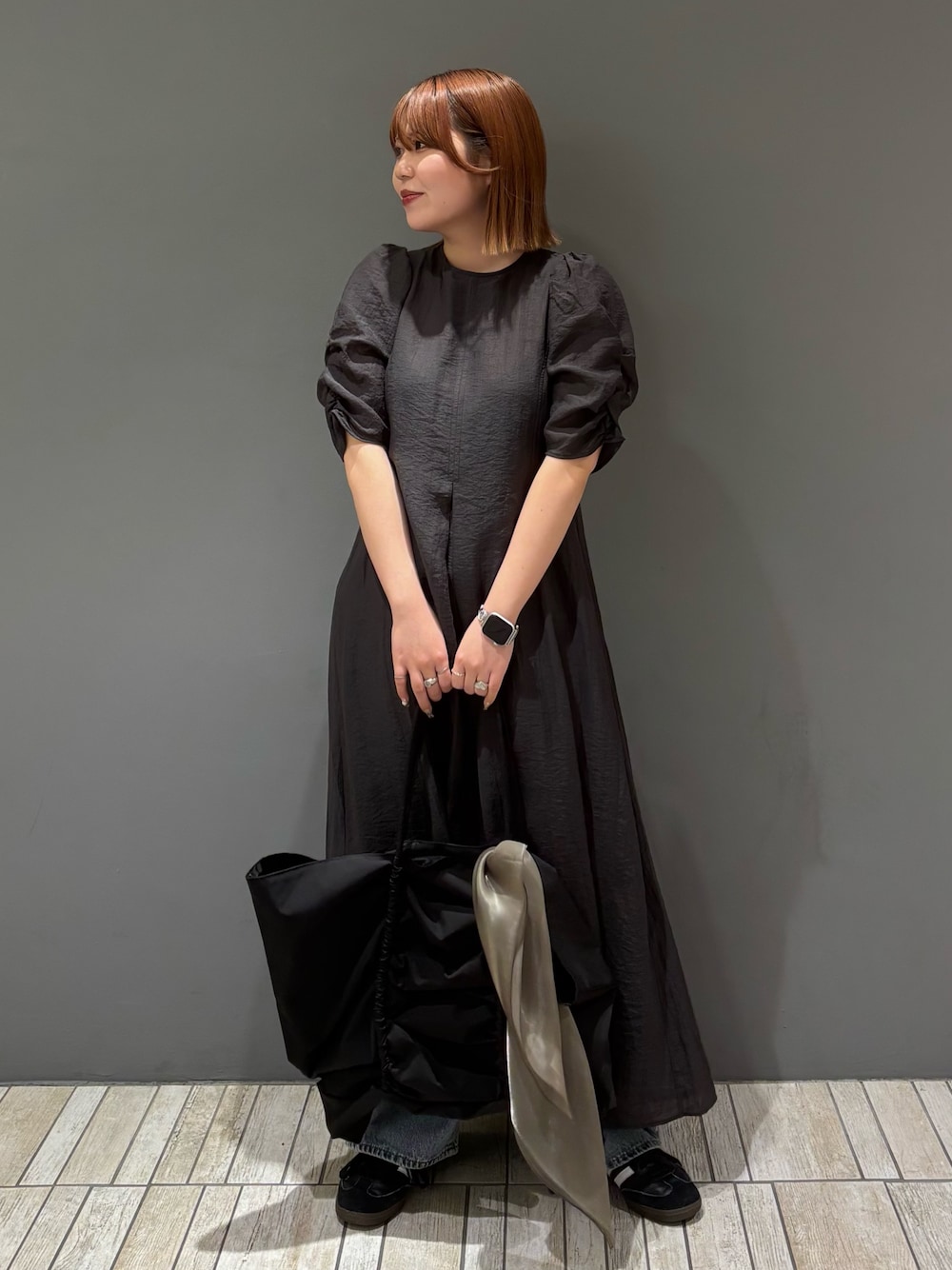 ブラック系のショルダーバッグ、ブルー系のデニムパンツ、グレー系のワンピースを着用したレディースの春コーディネートの1枚目の写真