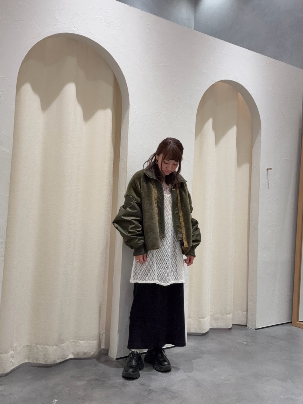 グリーン系のブルゾン、ブラック系のスカート、ホワイト系のキャミソールを着用したレディースの秋コーディネートの1枚目の写真