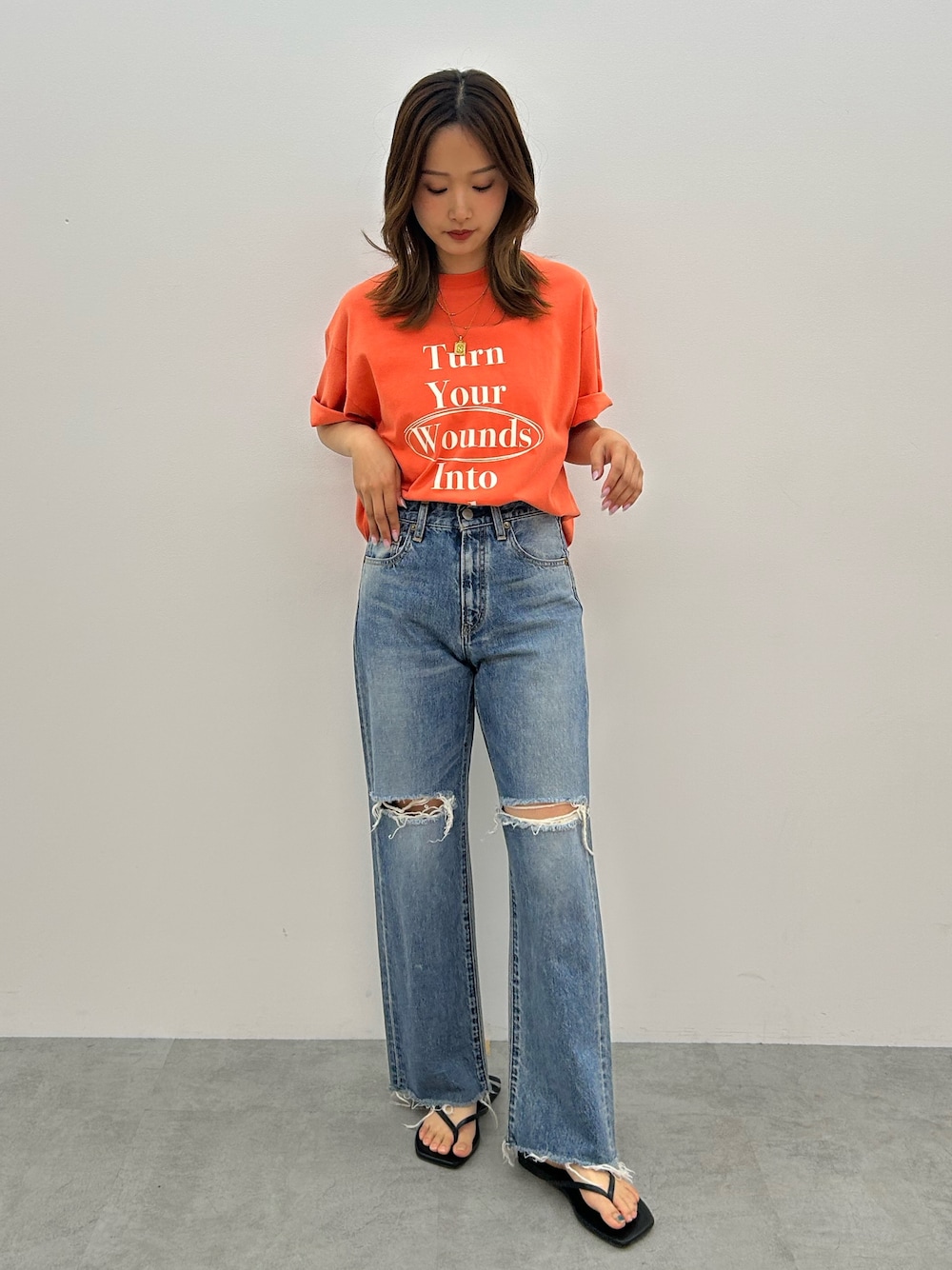 ブルー系のデニムパンツ、オレンジ系のTシャツ/カットソー、ブラック系のサンダルを着用したレディースの春コーディネートの1枚目の写真
