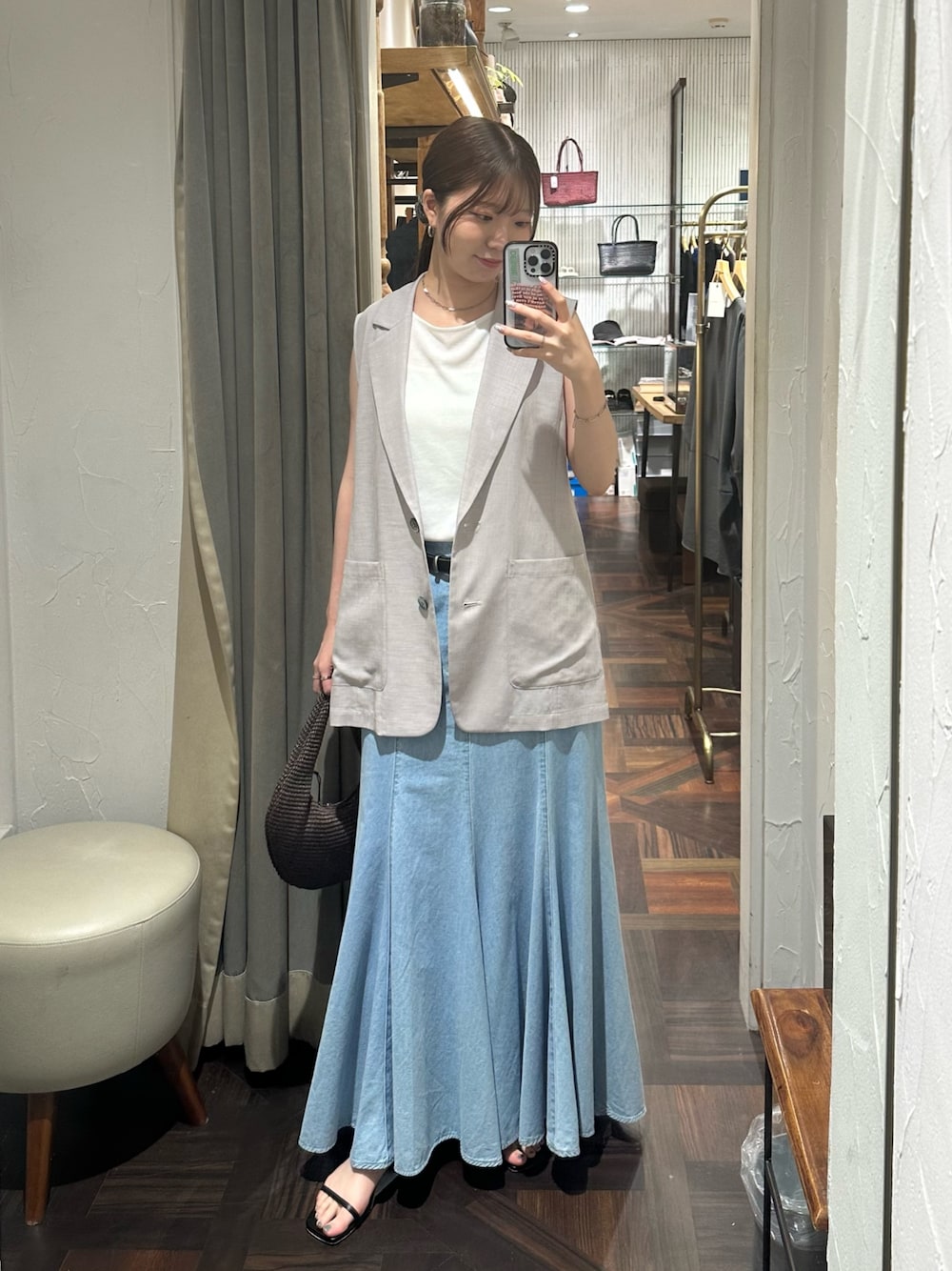 ブルー系のスカート、グレー系のベスト、ブラック系のサンダルを着用したレディースの夏コーディネートの1枚目の写真