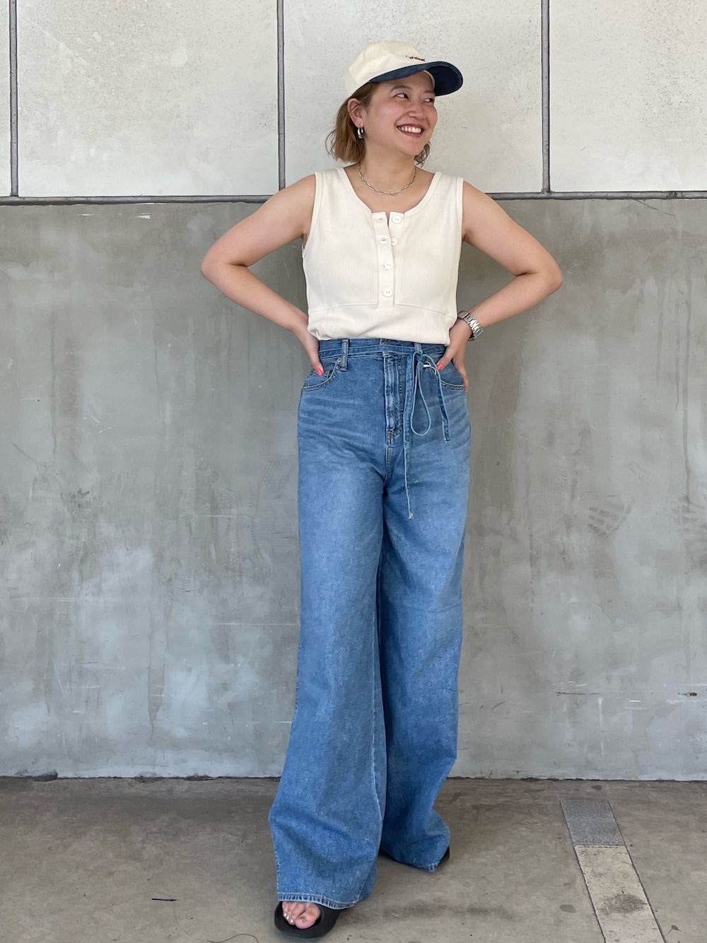 ブルー系のデニムパンツ、ホワイト系のタンクトップ、ホワイト系のキャップを着用したレディースの夏コーディネートの1枚目の写真