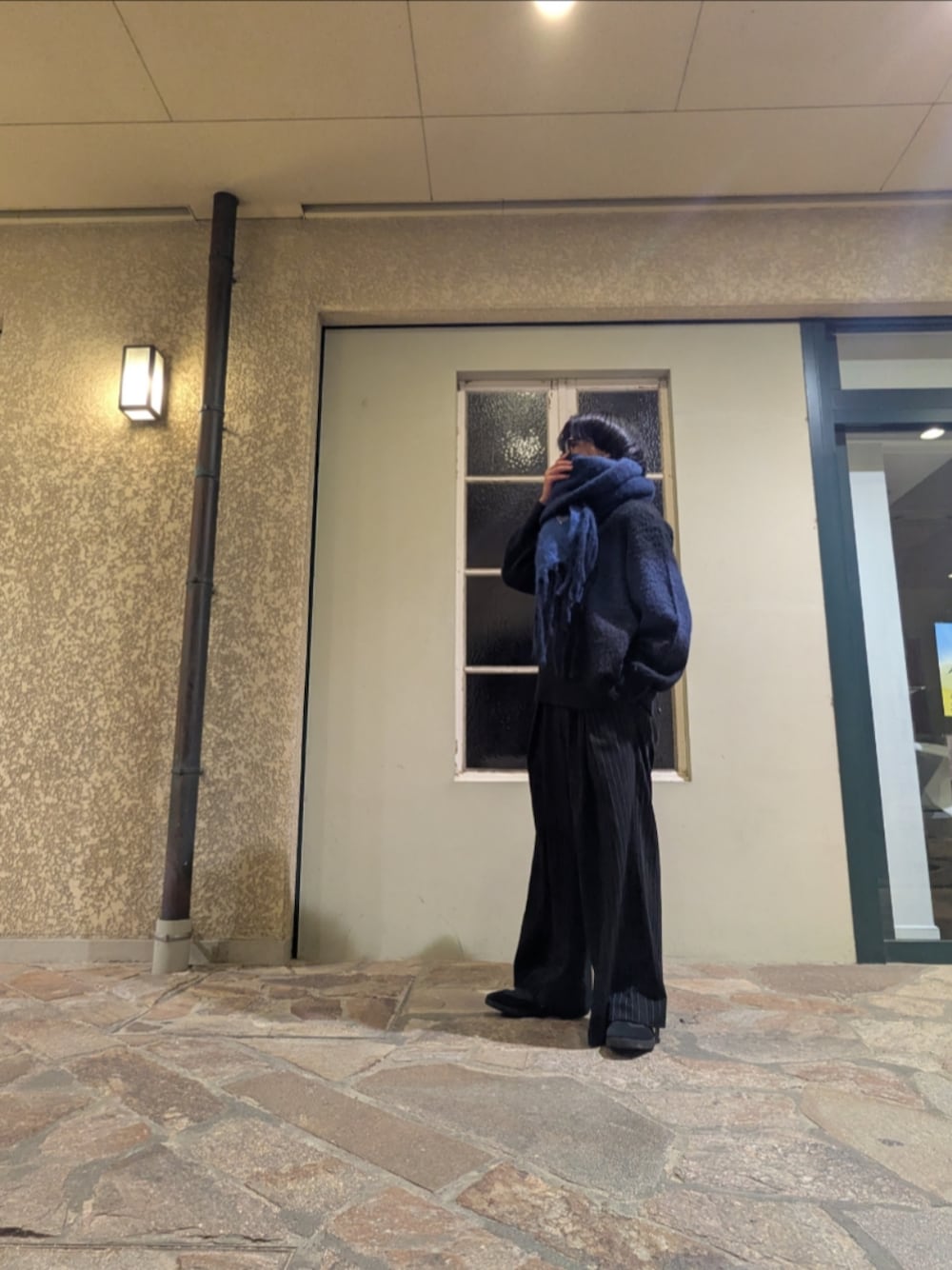 ブラック系のニット/セーター、ブラック系のスラックス、ブルー系のマフラーを着用したメンズの秋コーディネートの1枚目の写真