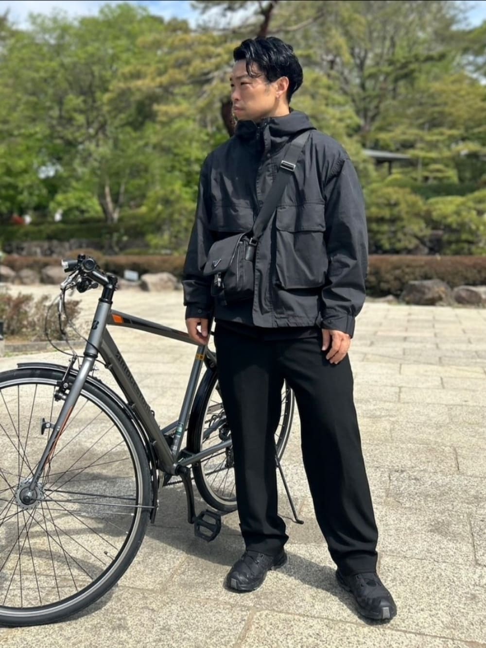 ブラック系のマウンテンパーカー、ブラック系のショルダーバッグ、ブラック系のスラックスを着用したメンズの春コーディネートの1枚目の写真