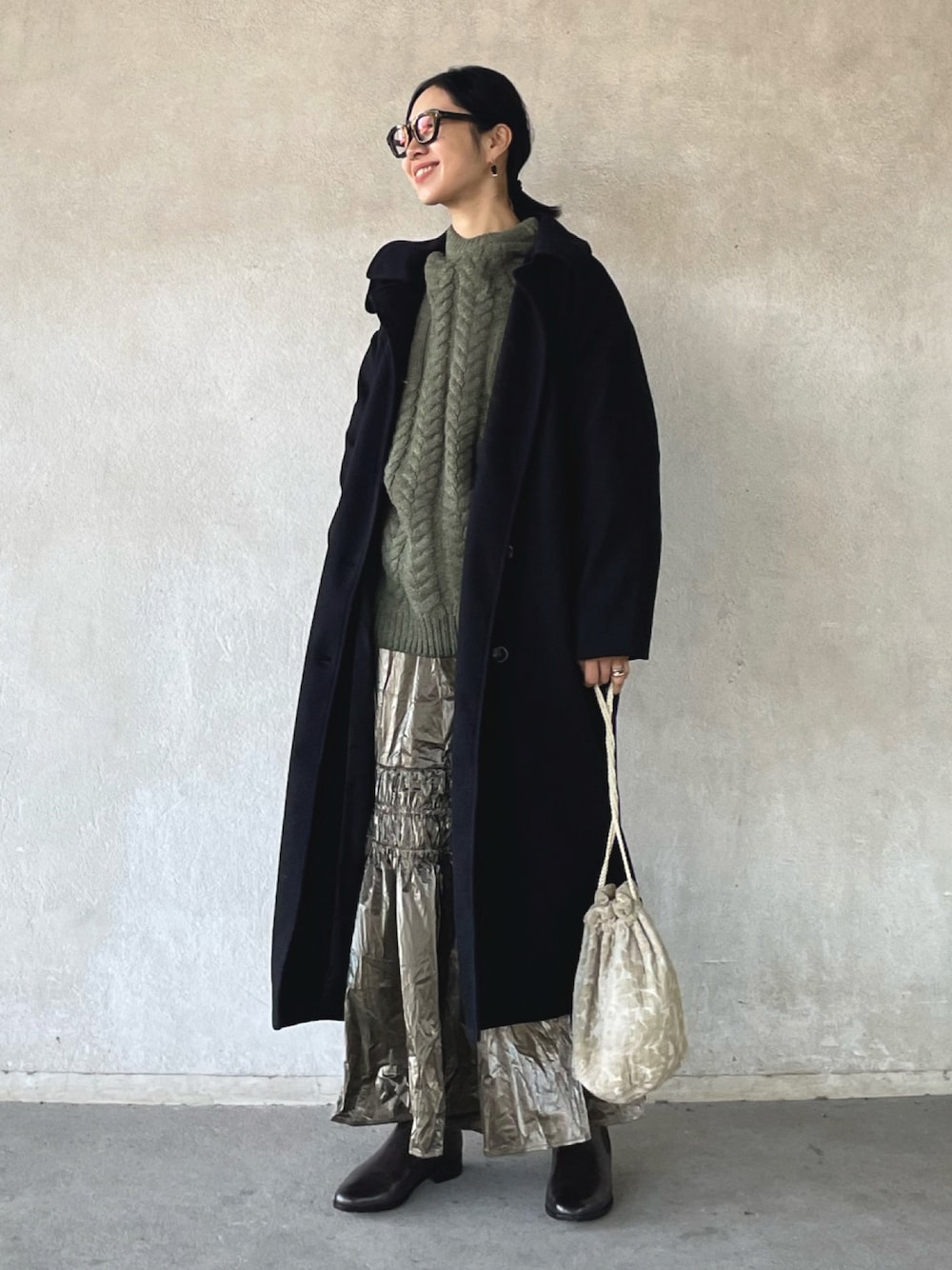 ブラック系のステンカラーコート、グリーン系のニット/セーター、シルバー系のスカートを着用したレディースの冬コーディネートの1枚目の写真