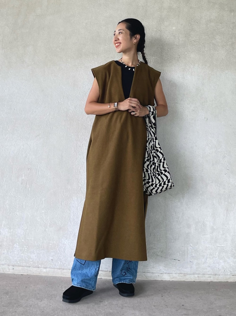 グリーン系のワンピース、ブラック系のモカシン/デッキシューズ、ブルー系のデニムパンツを着用したレディースの秋コーディネートの1枚目の写真