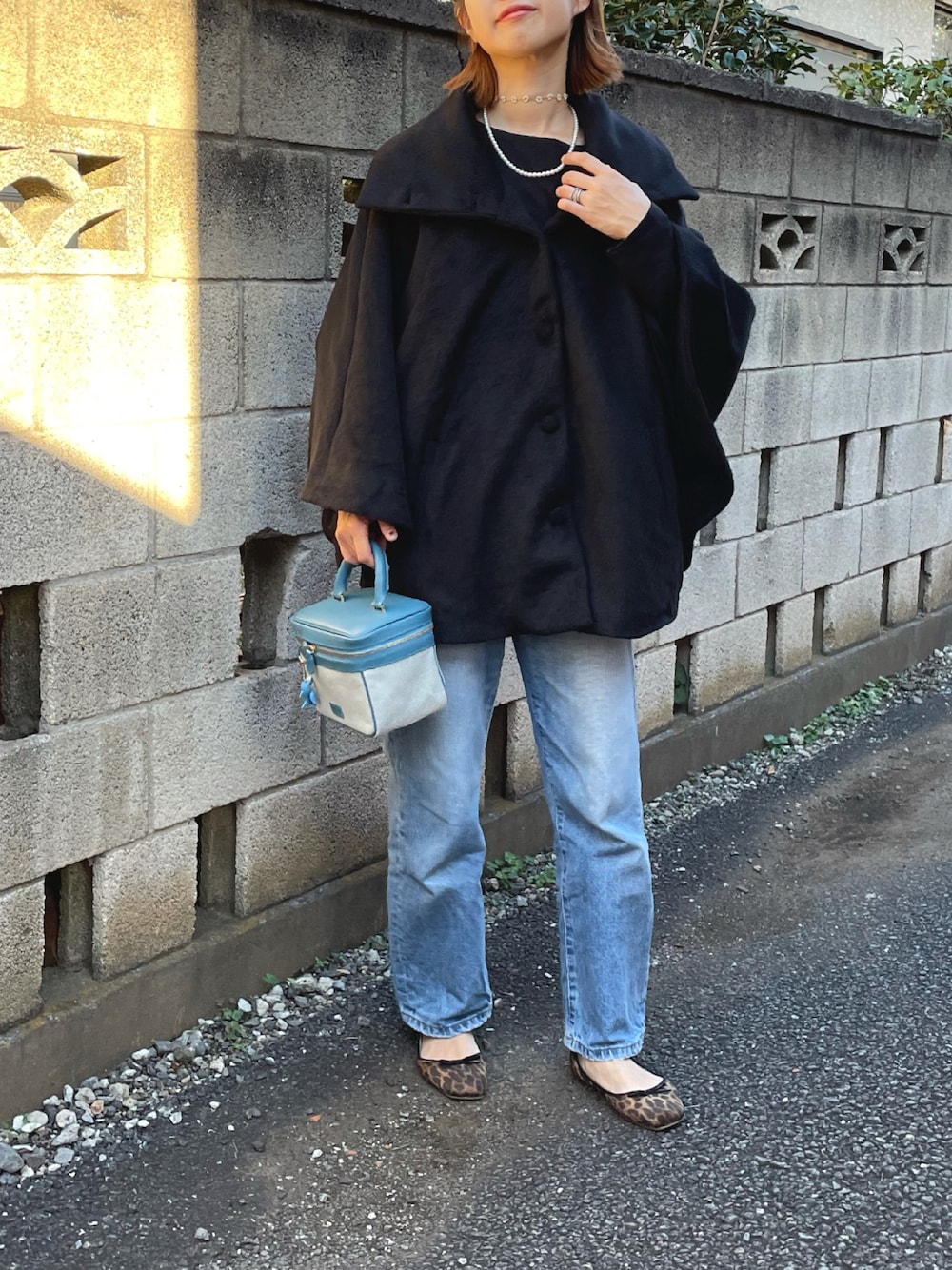 ブラック系のポンチョ、ブルー系のハンドバッグ、ブルー系のデニムパンツを着用したレディースの秋コーディネートの1枚目の写真
