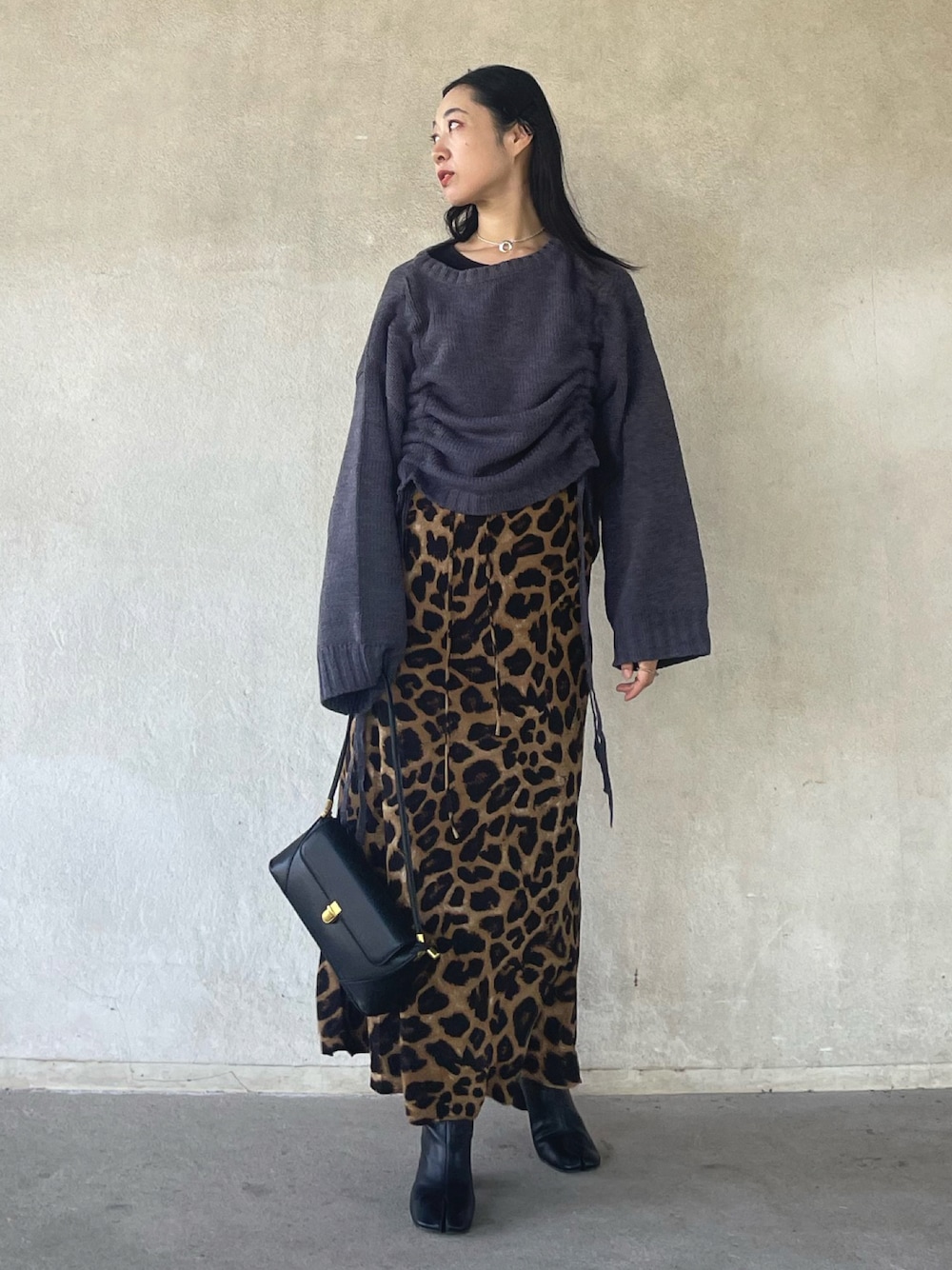 グレー系のニット/セーター、ベージュ系のスカート、ブラック系のハンドバッグを着用したレディースの秋コーディネートの1枚目の写真