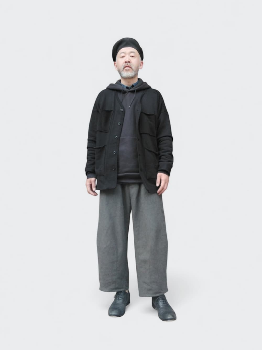 グレー系のパンツ、ブラック系のカーディガン/ボレロ、ブラック系のハンチング/ベレー帽を着用したメンズの春コーディネートの1枚目の写真