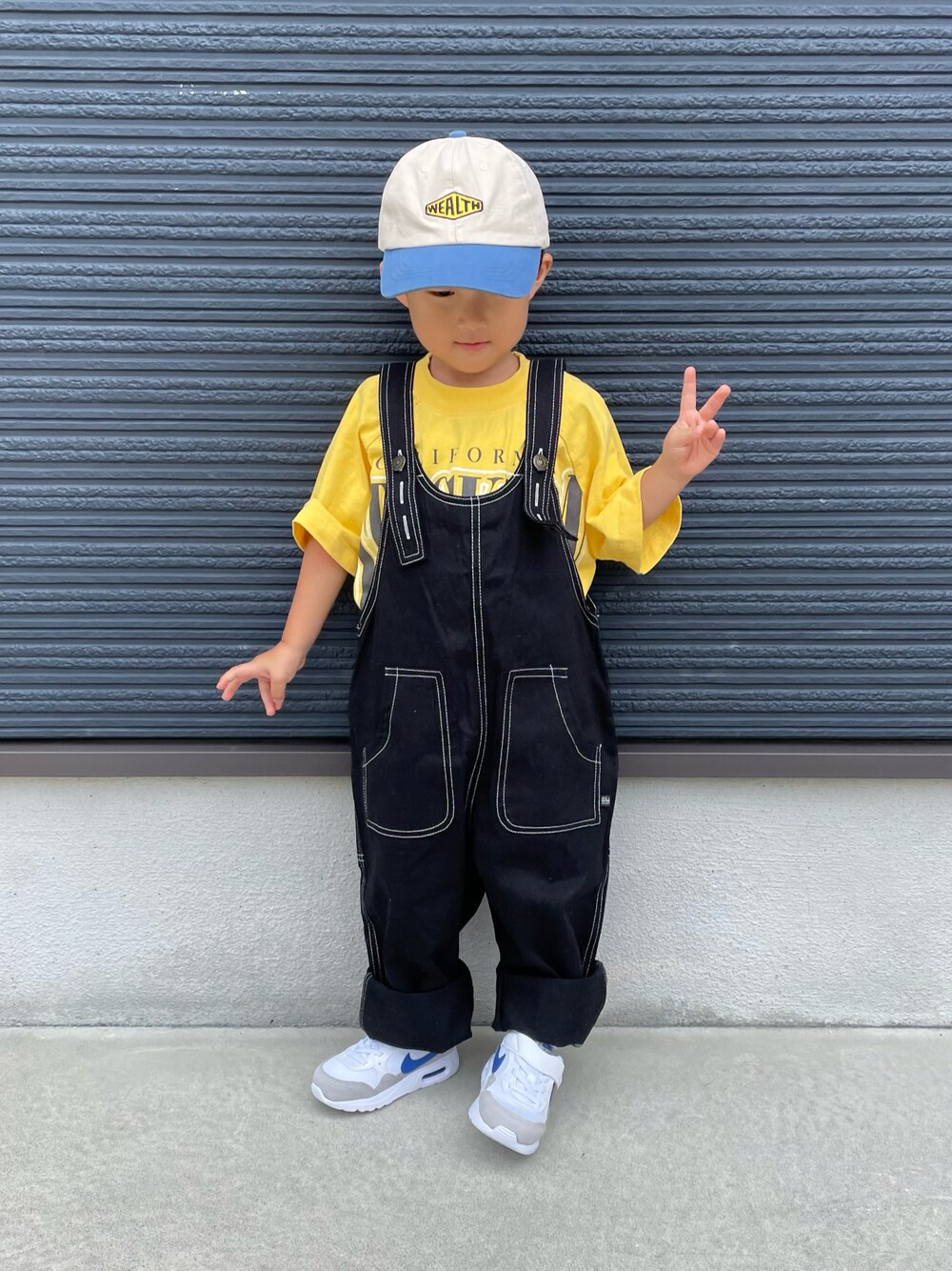 イエロー系のTシャツ/カットソー、ブラック系のサロペット/オーバーオール、ホワイト系のスニーカーを着用したキッズの秋コーディネートの1枚目の写真