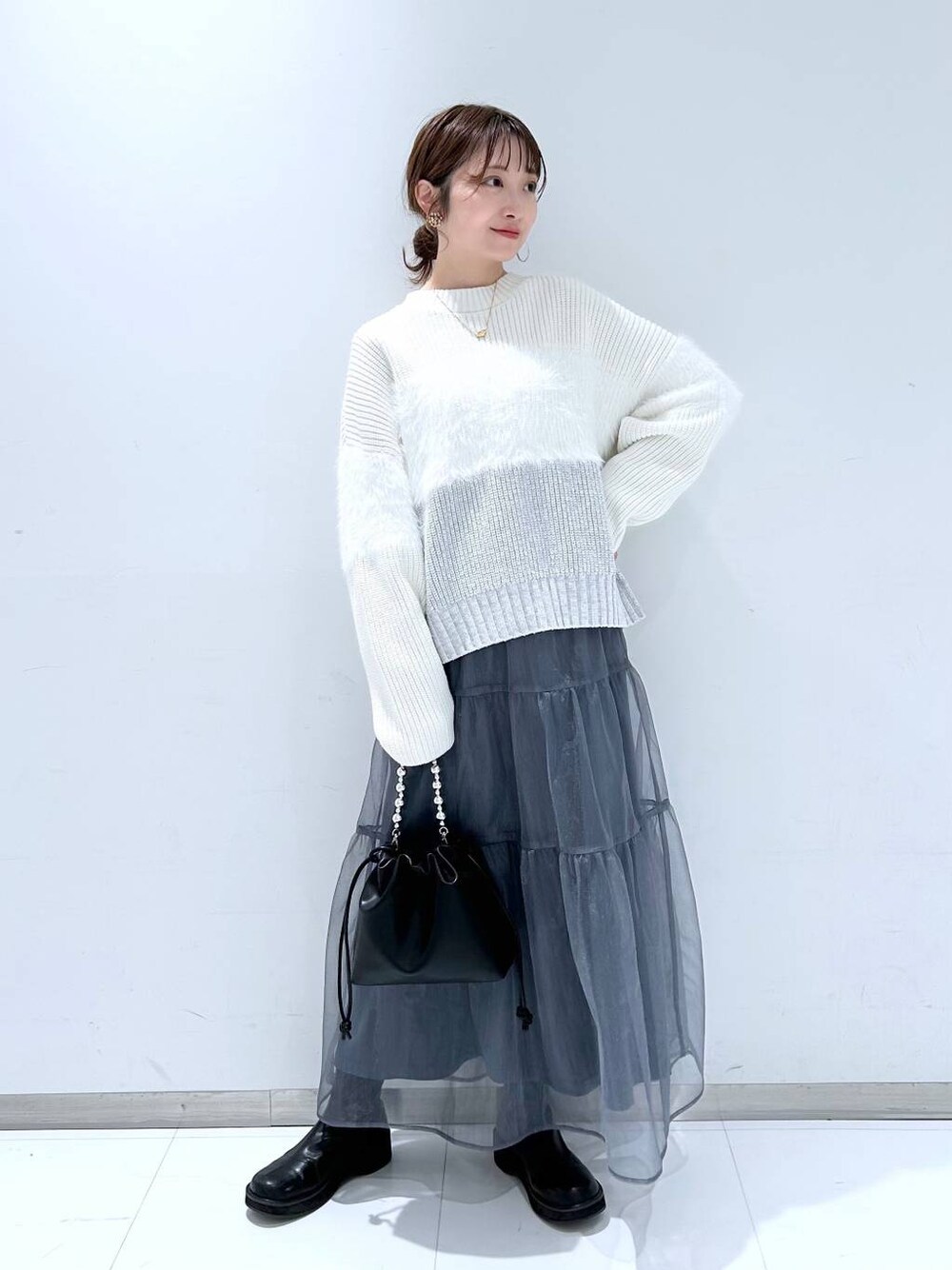 ブラック系のブーツ、ホワイト系のニット/セーター、グレー系のスカートを着用したレディースの冬コーディネートの1枚目の写真