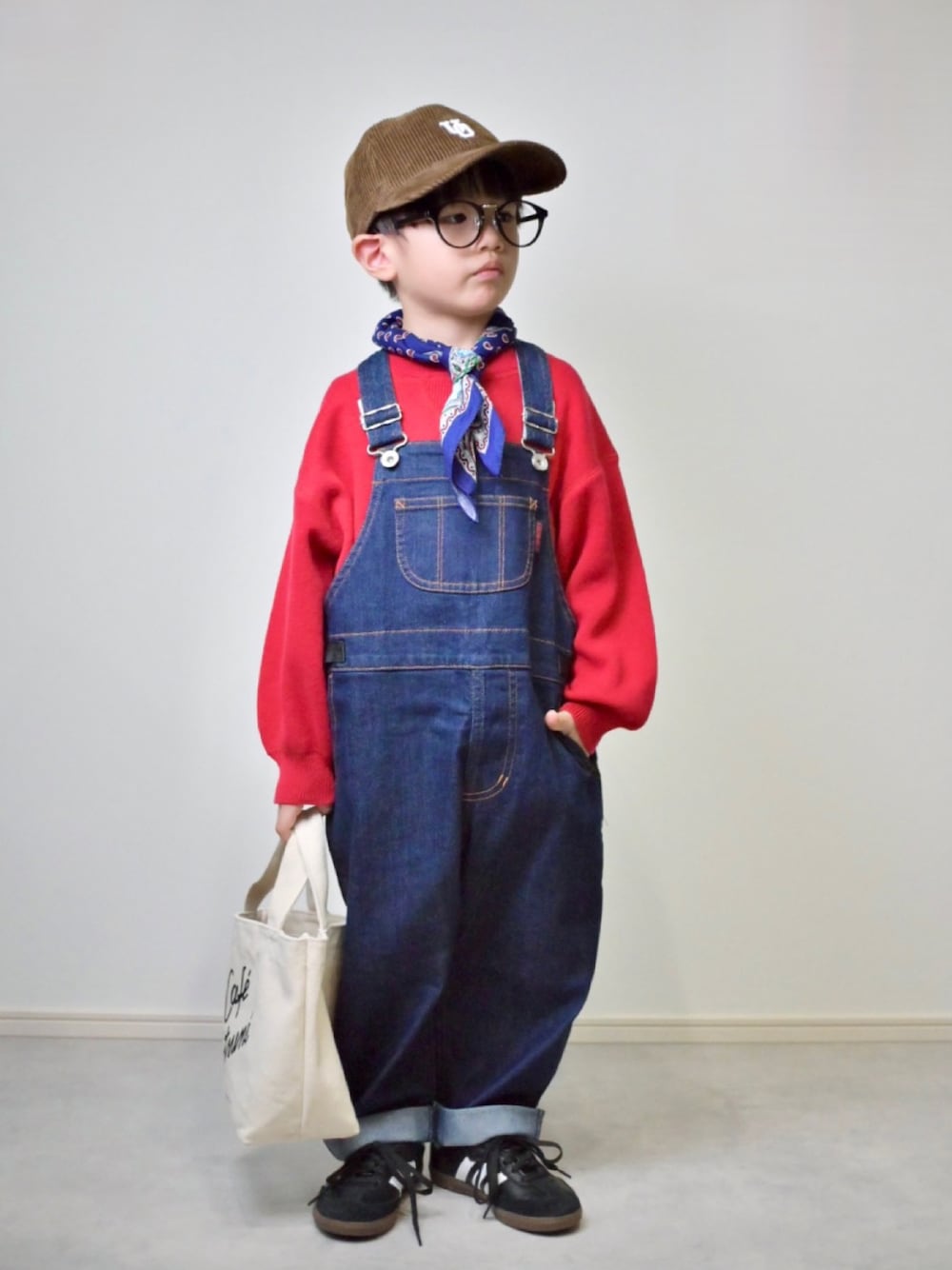 レッド系のニット/セーター、ブルー系のサロペット/オーバーオール、ブラック系のスニーカーを着用したキッズの秋コーディネートの1枚目の写真