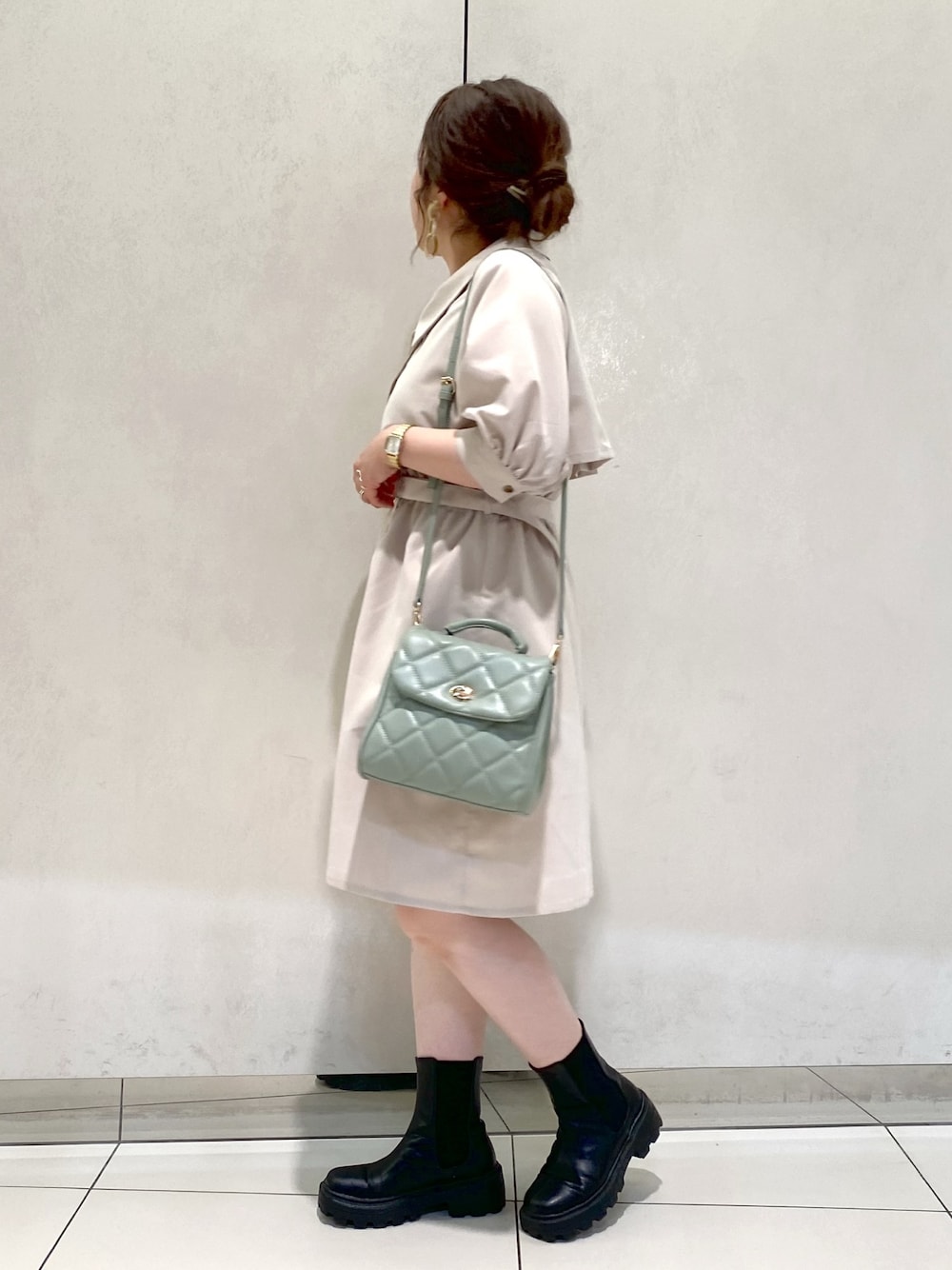 ベージュ系のワンピース、ブラック系のブーツ、グリーン系のショルダーバッグを着用したレディースの春コーディネートの2枚目の写真