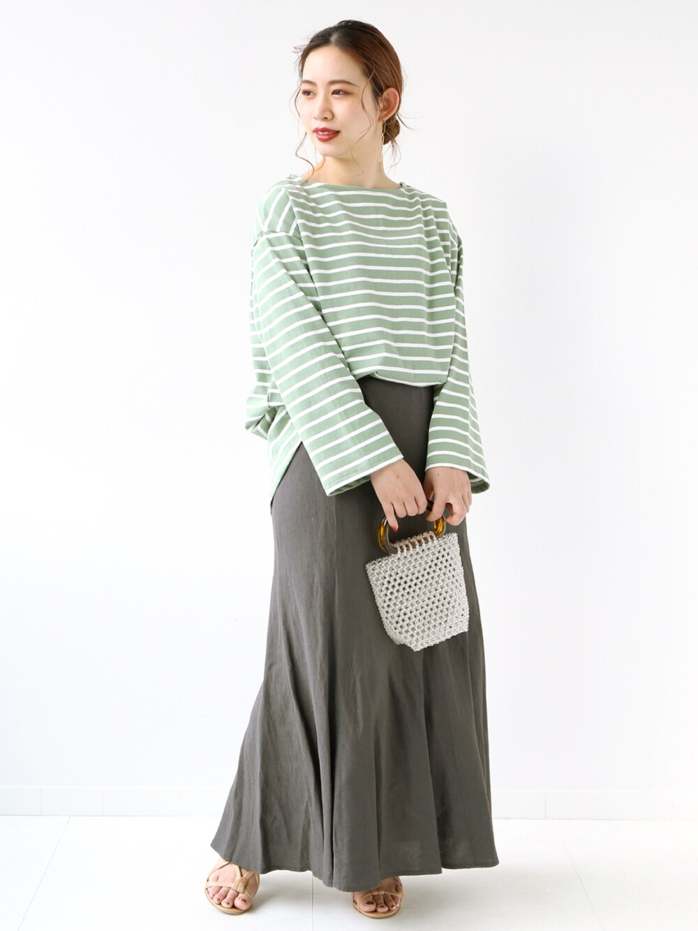 ホワイト系のハンドバッグ、グレー系のスカート、グリーン系のTシャツ/カットソーを着用したレディースの夏コーディネートの1枚目の写真