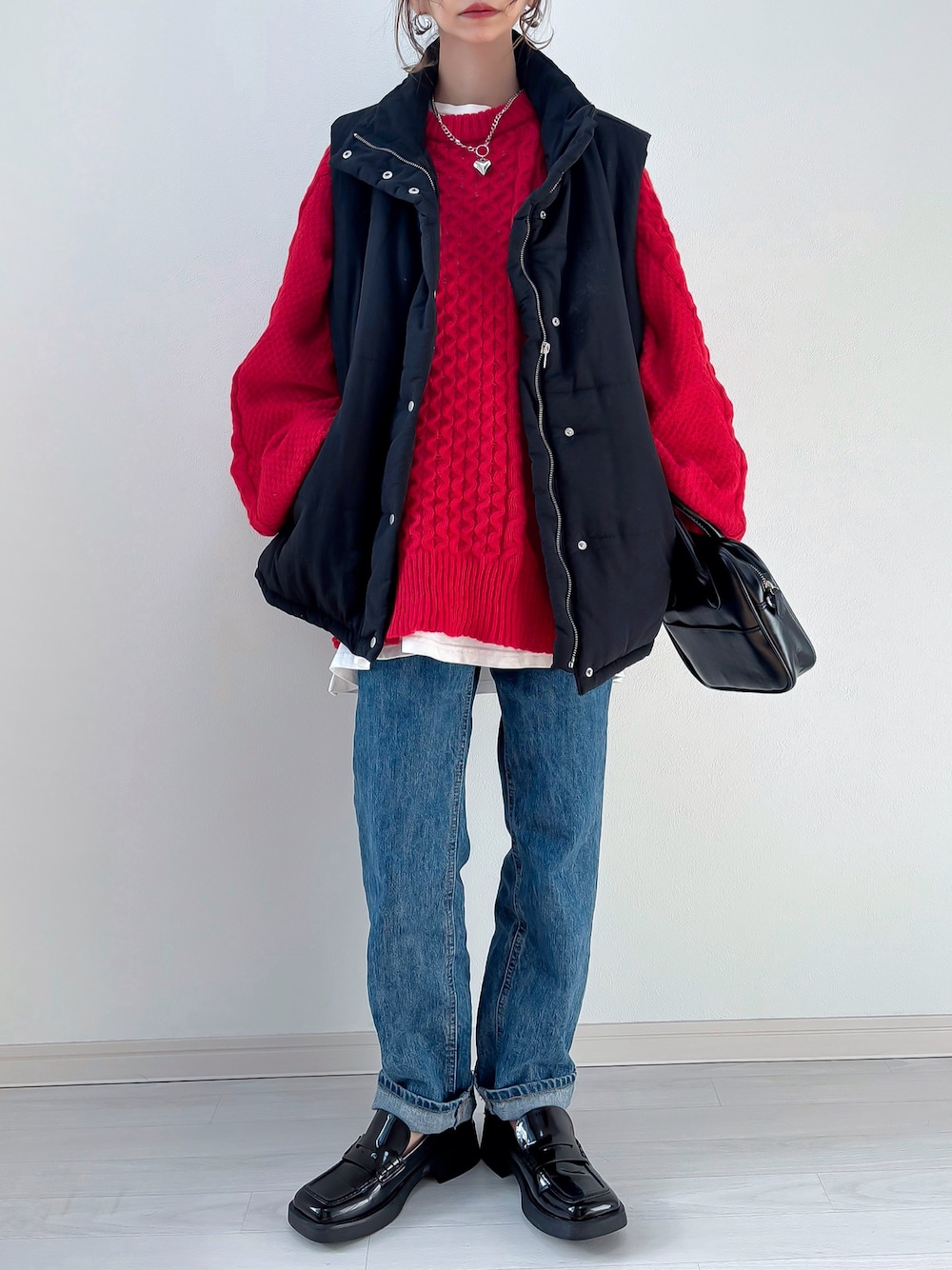 ブラック系のベスト、レッド系のニット/セーター、ブルー系のデニムパンツを着用したレディースの冬コーディネートの1枚目の写真