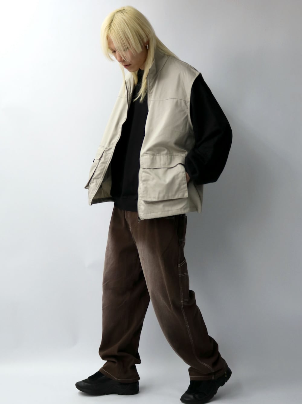 ホワイト系のベスト、ブラック系のスウェット、ブラウン系のデニムパンツを着用したメンズの春コーディネートの1枚目の写真