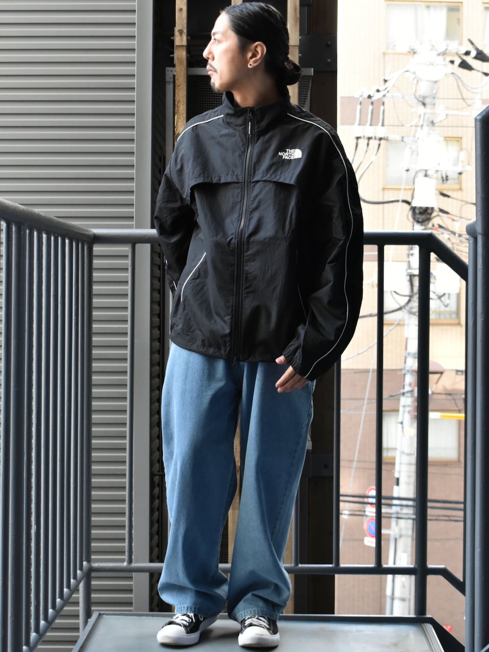 ブラック系のナイロンジャケット、ブルー系のデニムパンツ、ブラック系のスニーカーを着用したメンズの春コーディネートの1枚目の写真