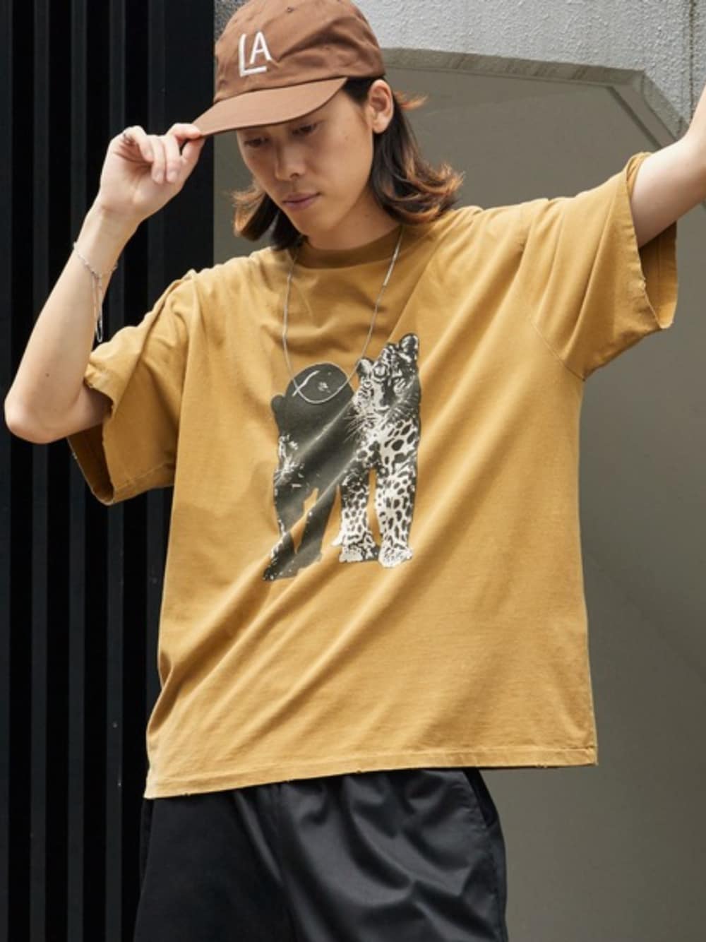 ブラック系のデニムパンツ、グリーン系のTシャツ/カットソー、ブラウン系のキャップを着用したメンズの夏コーディネートの1枚目の写真