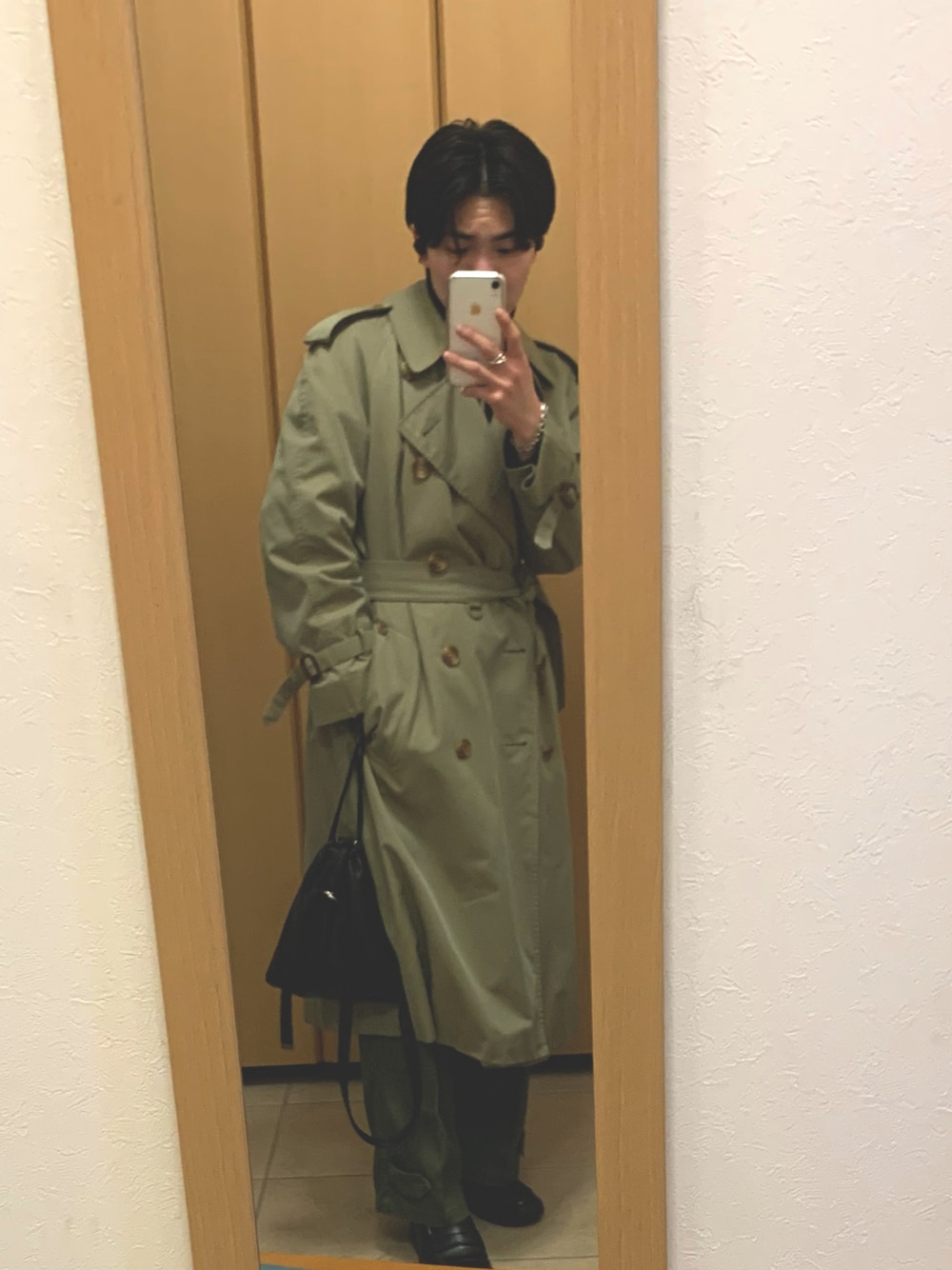 ベージュ系のトレンチコート、ブラック系のニット/セーター、ブラック系のショルダーバッグを着用したメンズの冬コーディネートの1枚目の写真