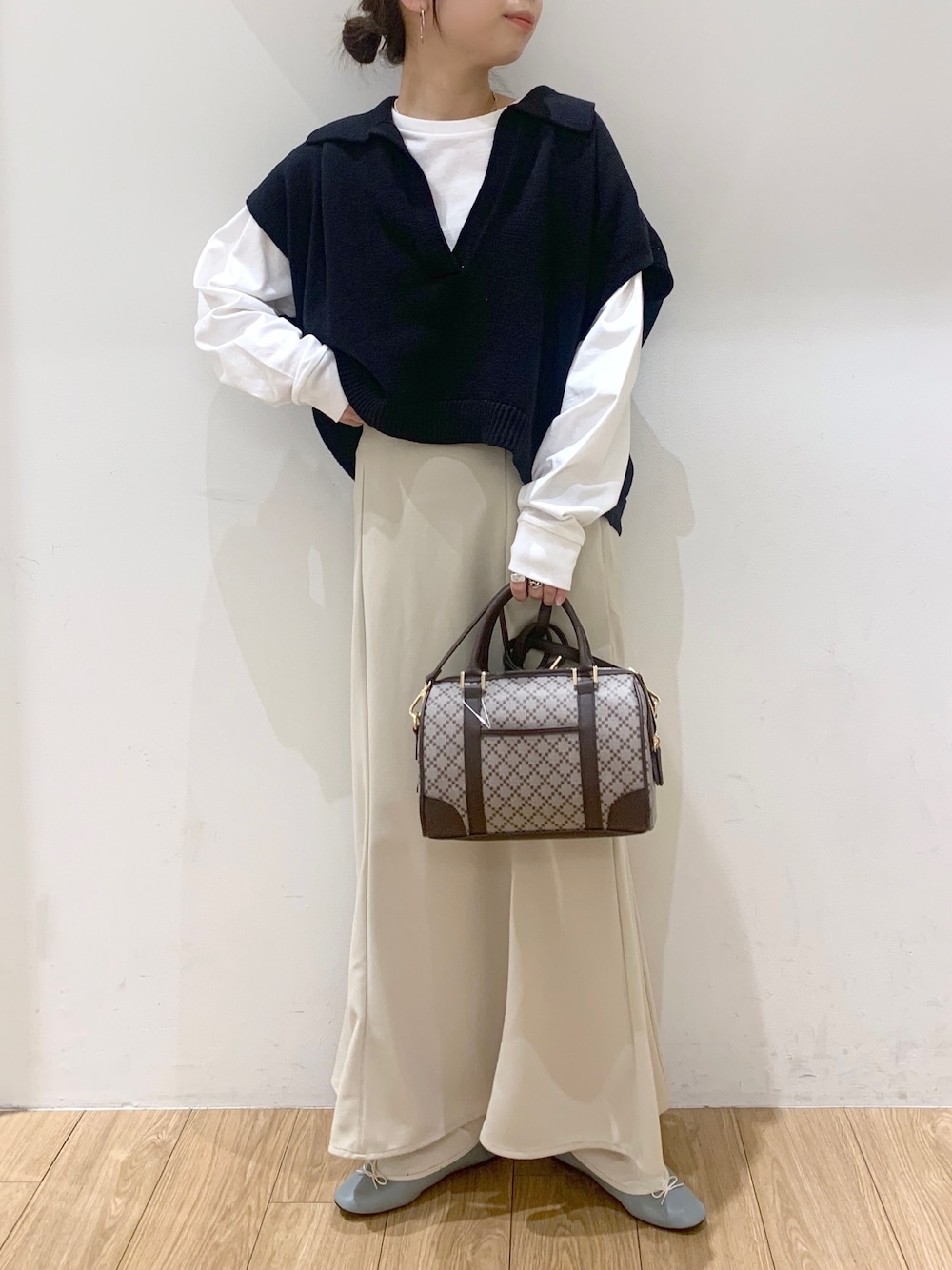 ホワイト系のスカート、ブラック系のベスト、ブルー系のバレエシューズを着用したレディースの春コーディネートの2枚目の写真