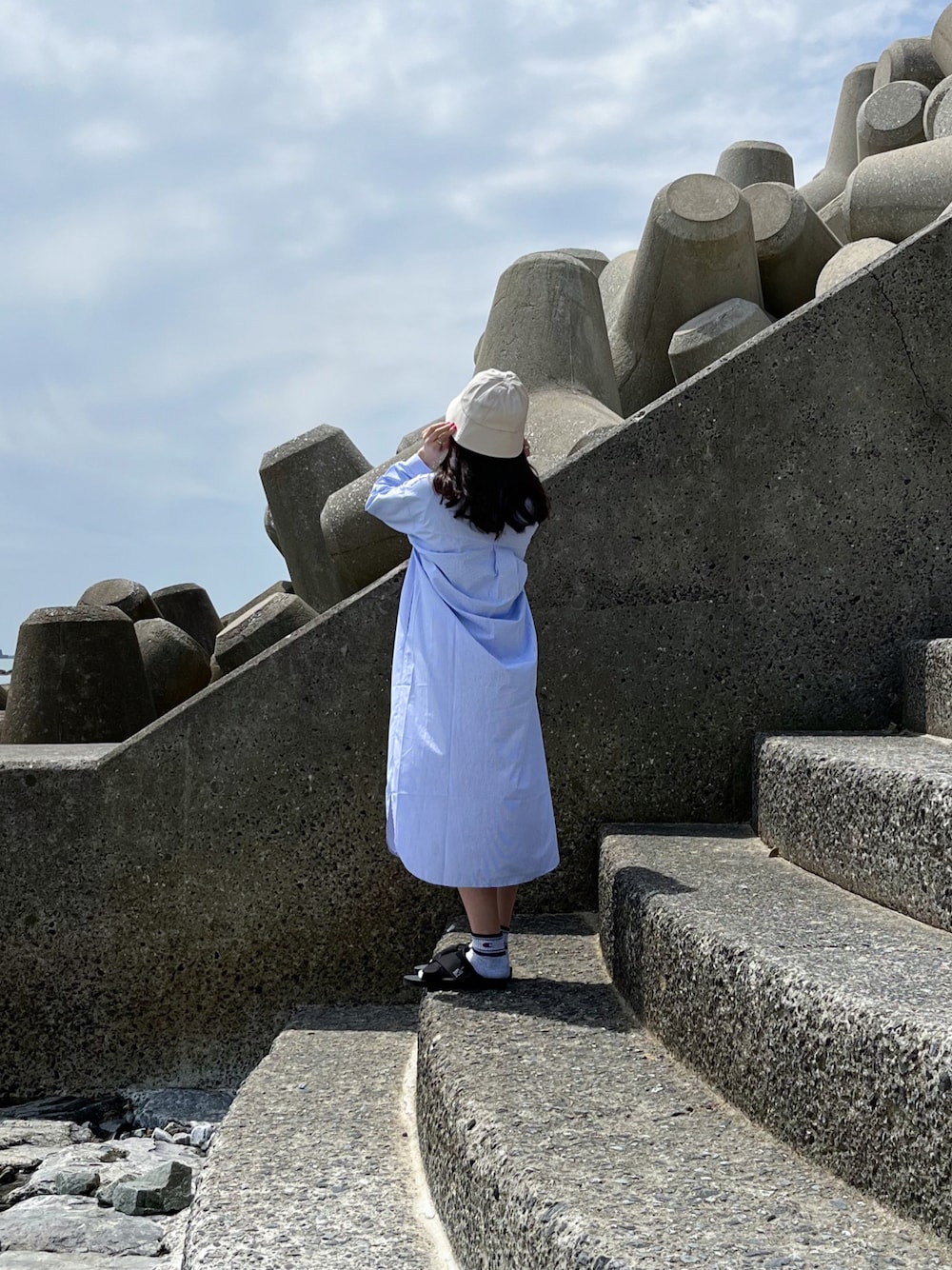 ブルー系のシャツワンピース、ブラック系のサンダル、ベージュ系のハットを着用したレディースの春コーディネートの1枚目の写真