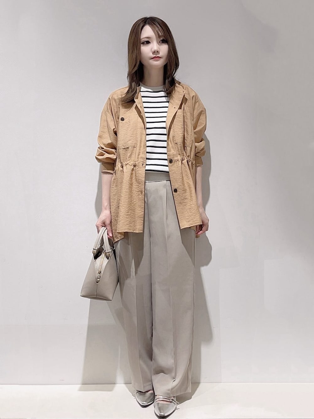 グレー系のハンドバッグ、シルバー系のパンプス、ホワイト系のニット/セーターを着用したレディースの春コーディネートの1枚目の写真