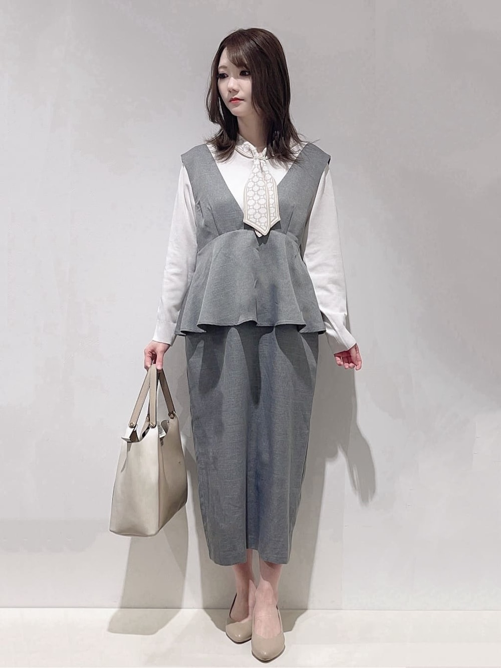 グレー系のワンピース、ホワイト系のニット/セーター、ベージュ系のトートバッグを着用したレディースの春コーディネートの1枚目の写真