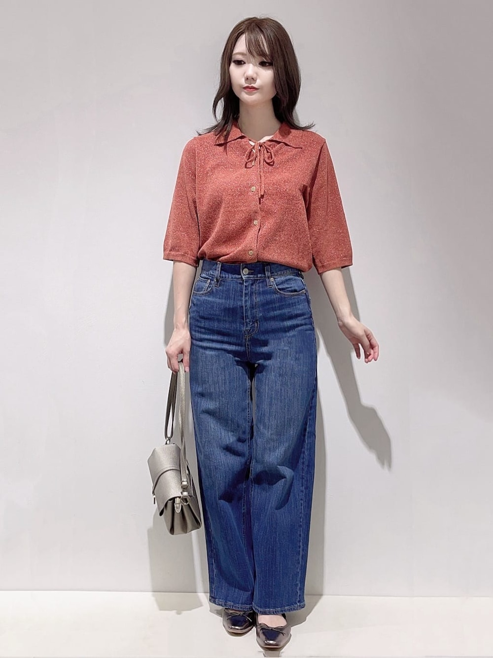 レッド系のニット/セーター、ブルー系のデニムパンツ、シルバー系のショルダーバッグを着用したレディースの秋コーディネートの1枚目の写真