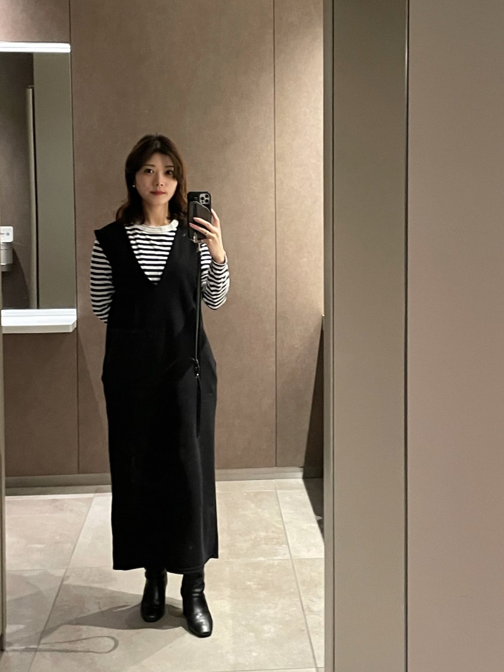 ブラック系のジャンパースカート、ブラック系のブーツ、ホワイト系のTシャツ/カットソーを着用したレディースの秋コーディネートの1枚目の写真