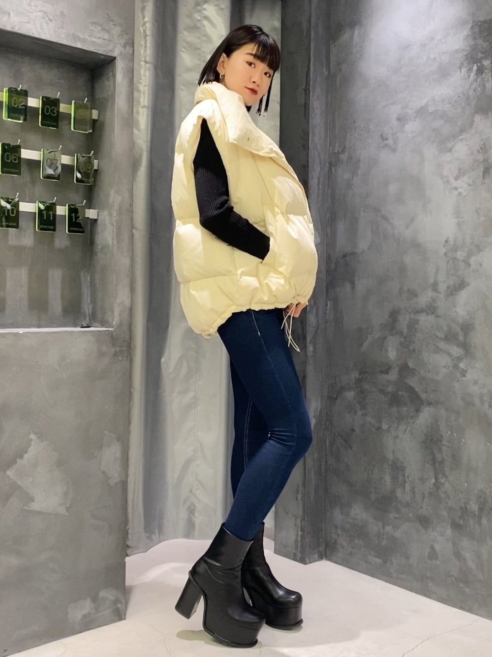 ブルー系のデニムパンツ、ブラック系のブーツ、ホワイト系のダウンベストを着用したレディースの秋コーディネートの1枚目の写真