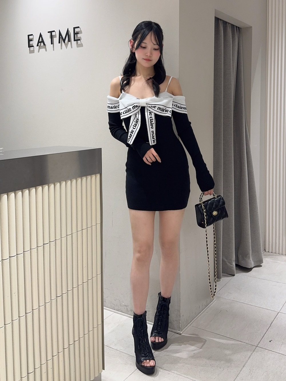 ブラック系のワンピース、ブラック系のハンドバッグ、ブラック系のブーツを着用したレディースの春コーディネートの1枚目の写真