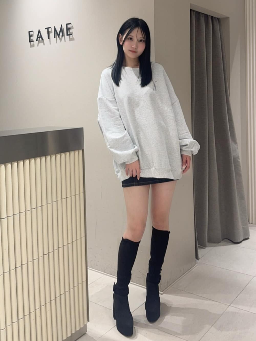 ブラック系のデニムスカート、ブラック系のブーツ、グレー系のスウェットを着用したレディースの秋コーディネートの1枚目の写真