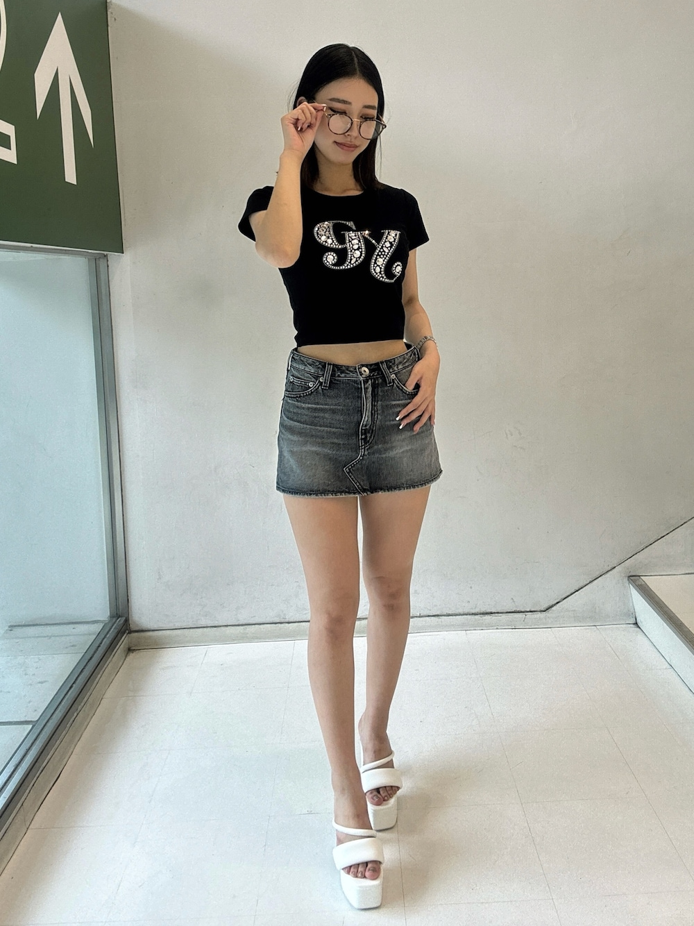 ブラック系のデニムスカート、ブラック系のTシャツ/カットソー、ホワイト系のサンダルを着用したレディースの夏コーディネートの1枚目の写真
