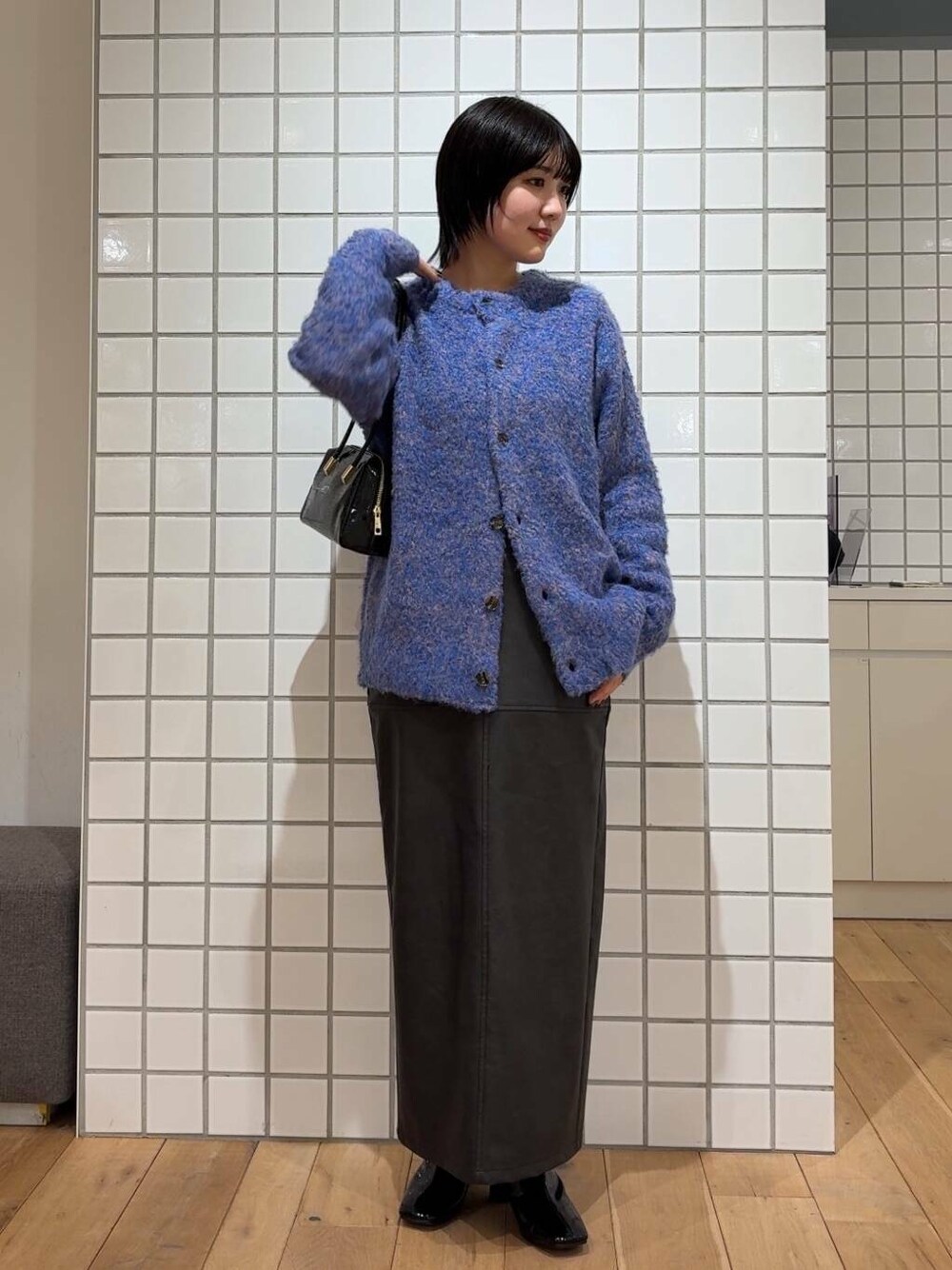 ブラック系のスカート、ブラック系のブーツ、ブラック系のハンドバッグを着用したレディースの冬コーディネートの1枚目の写真